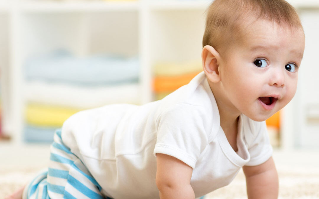 Smiling baby in a white onesie and blue-striped pants crawling on a soft carpet - www.ogallalanebraskainsurance.com/
